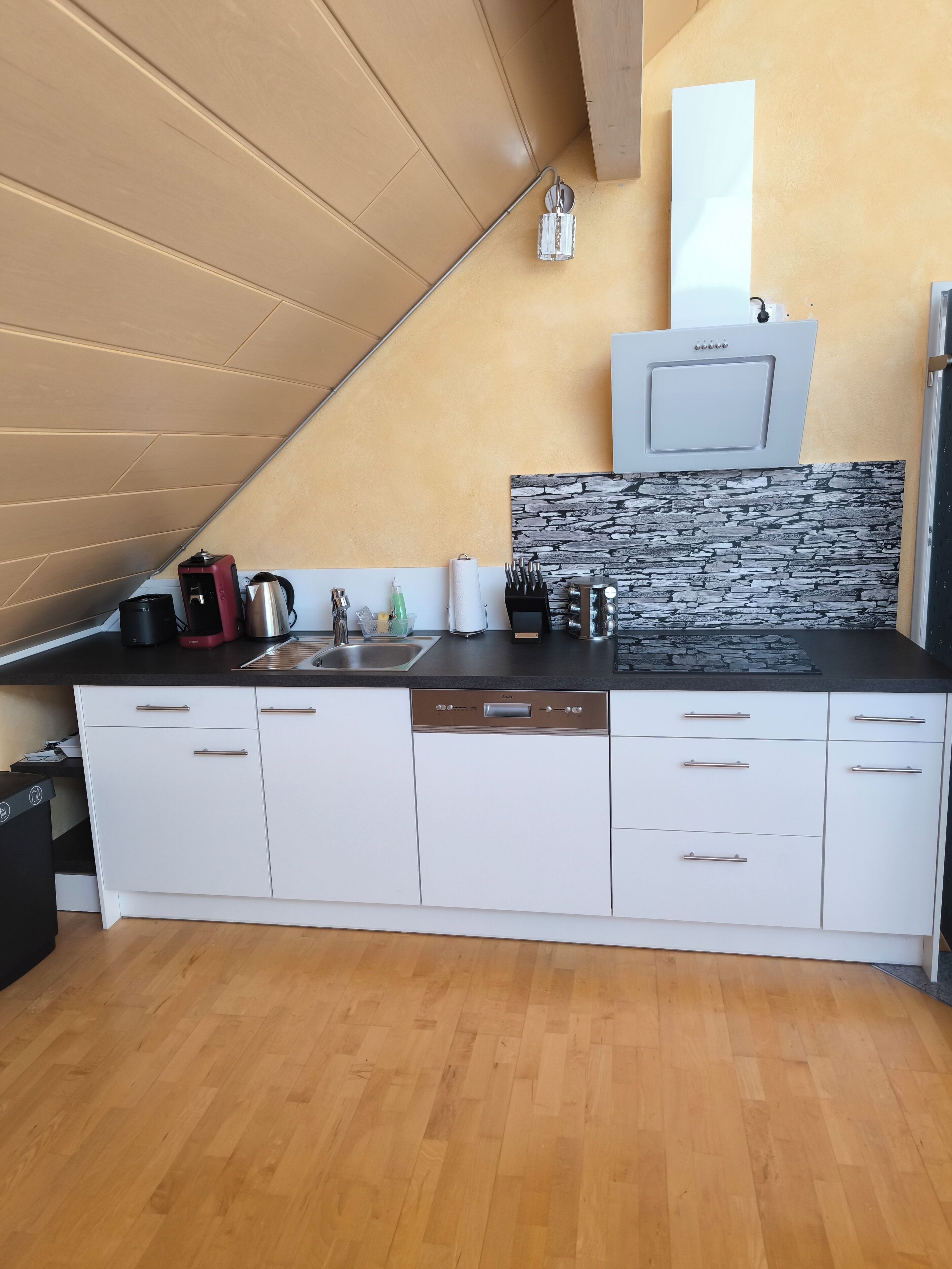 Eine moderne Küche mit weißen Schränken, einer schwarzen Arbeitsplatte und einer Rückwand aus Stein.