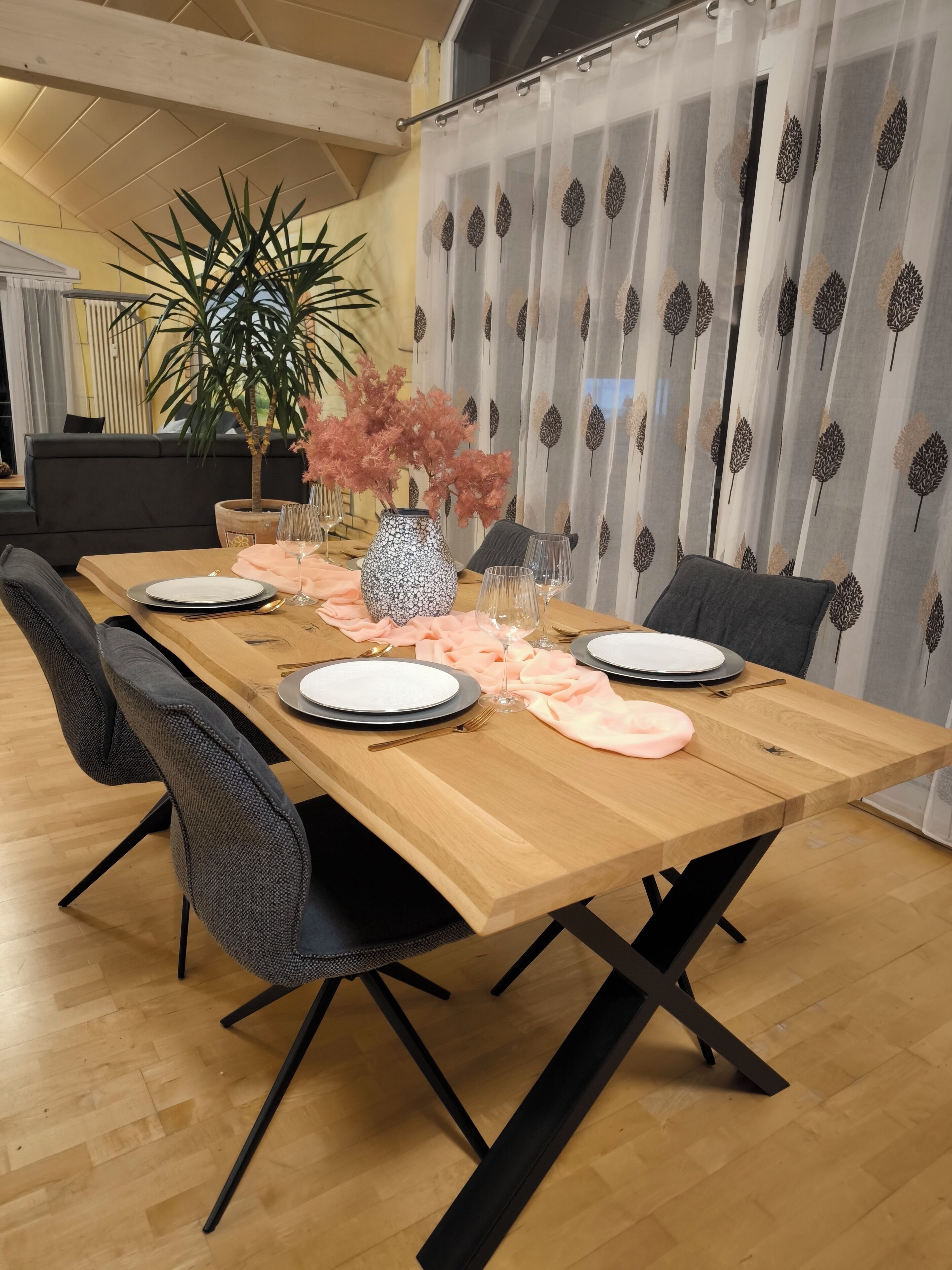 Ein Essbereich mit einem Holztisch, gedeckt für vier Personen, schwarzen Stühlen und einer Vase mit rosafarbenen Blumen.