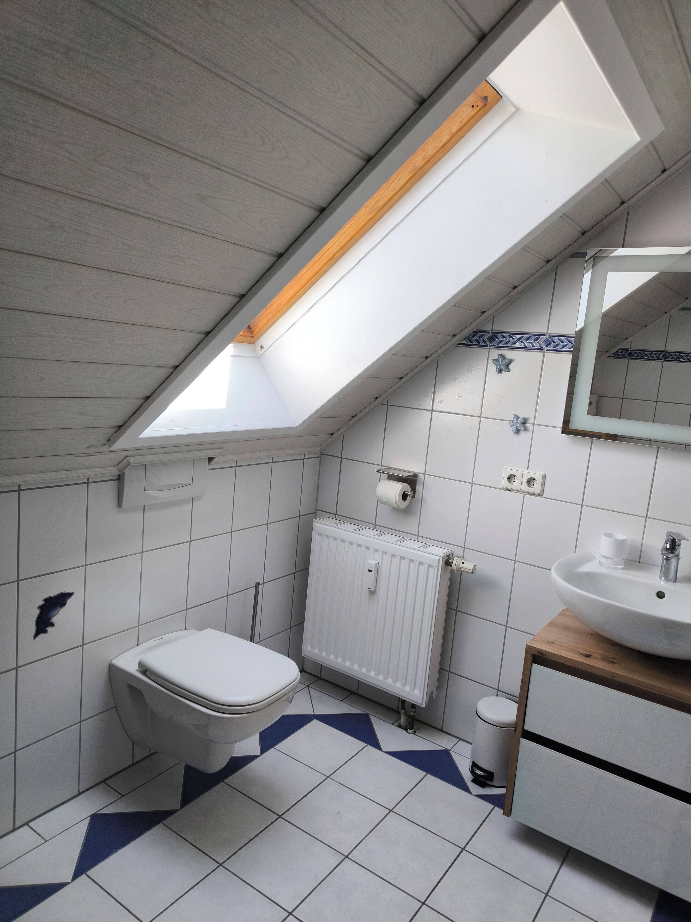 Een compacte, moderne badkamer met dakraam, witte tegels, toilet, wastafel en spiegel.