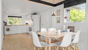 Una cocina moderna con armarios blancos, horno empotrado y microondas. Hay un comedor con una mesa redonda y sillas blancas.