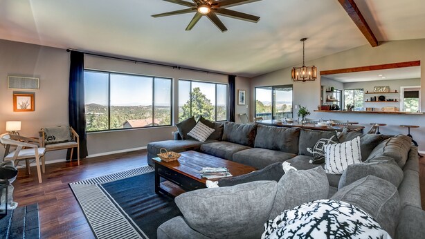 A spacious living room with a large window, a ceiling fan, and a dining area with a view. - 5BR Group Escape • Game Room • Views • Sleeps 12 • 10 mins to DT • EV charger (Prescott)