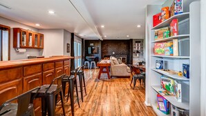 A modern kitchen with wooden cabinets, a bar area, and a bookshelf filled with board games. - 5BR Group Escape • Game Room • Views • Sleeps 12 • 10 mins to DT • EV charger (Prescott)
