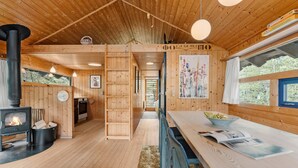 A cozy wooden cabin interior with a central fireplace, a dining area, and a view of the outdoors.