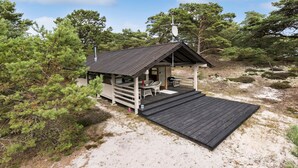 A small cabin with a porch, surrounded by trees and sand.
