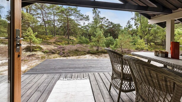 A wooden deck with a wicker chair and a table, overlooking a forested area.