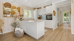 A modern kitchen with white cabinetry, a central island, and a dining area with wicker furniture. - Amazing home in Ebeltoft with WiFi (Ebeltoft)