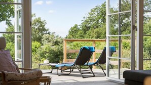 A sunlit patio with a wicker chair, a lounge chair with a blue towel, and a wooden deck. - Amazing home in Ebeltoft with WiFi (Ebeltoft)