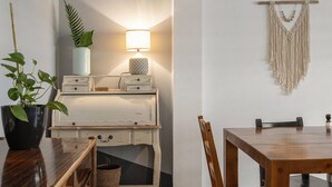 Ein Essbereich mit Holztisch und -stühlen, einem kleinen Schreibtisch mit Schubladen, einer Lampe und einer Wanddekoration aus Makramee.