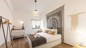 Ein modernes Schlafzimmer mit einem großen Bett, einem Nachttisch, einer Pendelleuchte und einem Wandteppich.