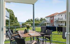 Ein überdachter Außenbereich mit Tisch und Stühlen, mit Blick auf eine Rasenfläche und ein Gebäude mit rotem Dach.