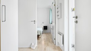 A narrow hallway with a bed, a radiator, and a small table with a lamp.