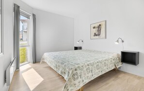 Ein Schlafzimmer mit einem Bett, zwei Nachttischen, einer Wandlampe, einem Fenster mit Vorhängen und einem gerahmten Bild an der Wand.