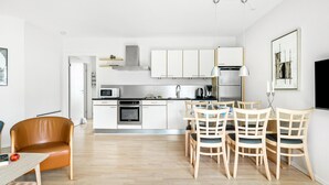 A modern kitchen with white cabinets, a microwave, oven, and a dining area with wooden chairs and a table.