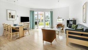 A modern living room with a wooden dining table, chairs, a sofa, and a TV.