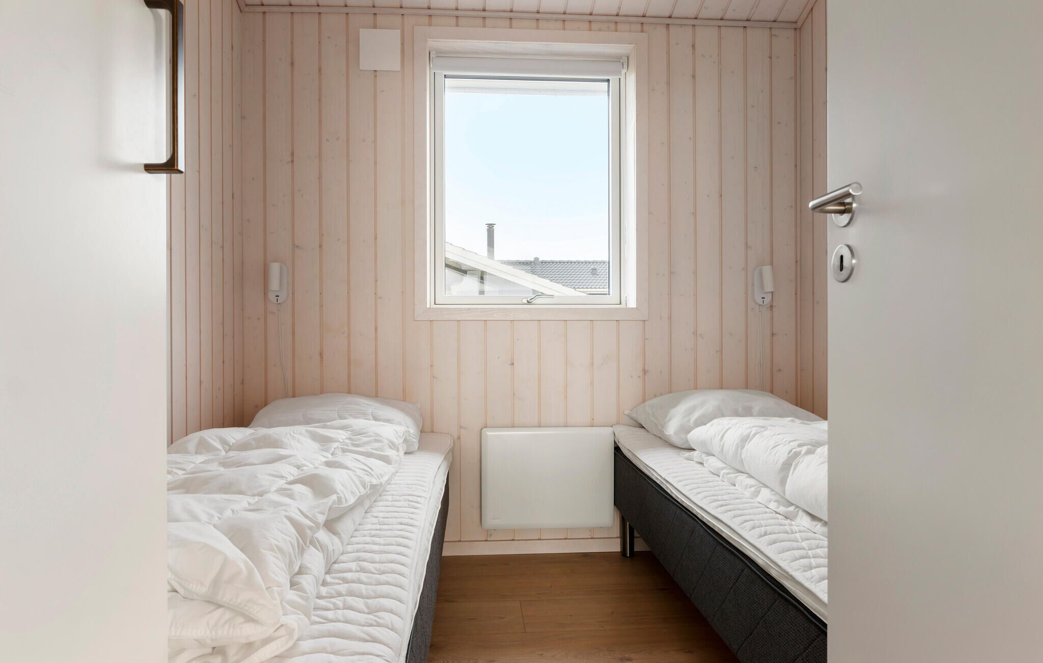 A small, single-room accommodation with two beds, a window, and a radiator.