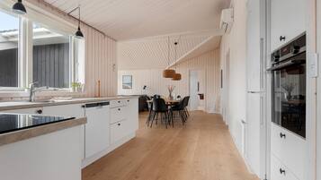 Une cuisine moderne avec des meubles blancs, un plancher en bois et des luminaires suspendus.