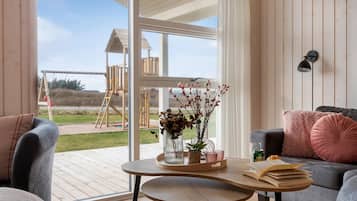 Un salon moderne avec une table en bois, un canapé et une grande fenêtre donnant sur un terrain de jeux et une plage.