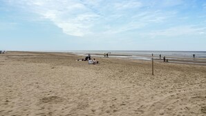 A wide sandy beach with a few people scattered along the shore.