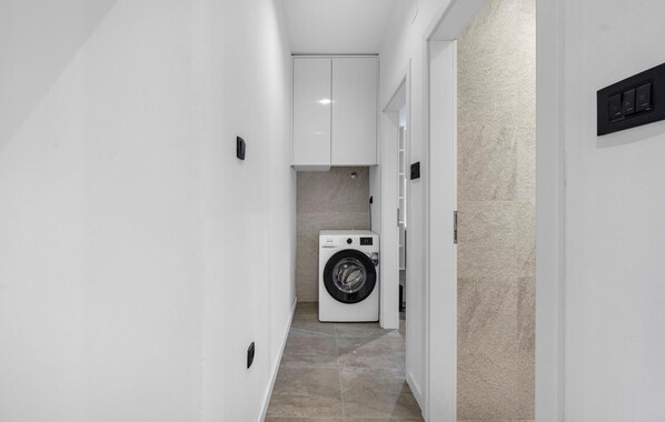 A narrow hallway with a washing machine in the center, white walls, and a tiled floor.