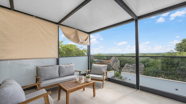 Un balcón con sofá, sillas y mesa, con vista a un paisaje pintoresco.