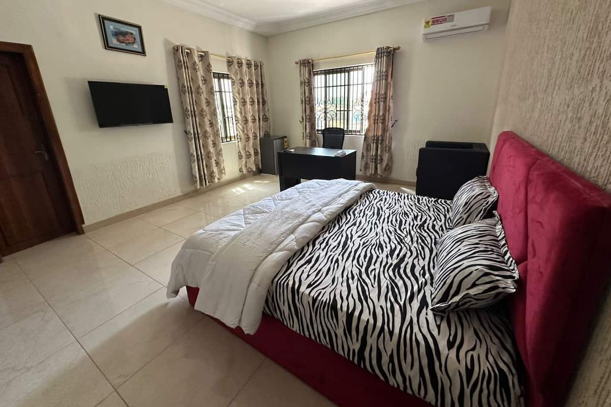 A bedroom with a bed, a desk, a chair, a TV, and curtains.