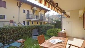A patio with a wooden table and chairs, a green chair, a black chair, and a small table with a towel. - Borgo delle Colline 19 by Wonderful Italy (Manerba del Garda)