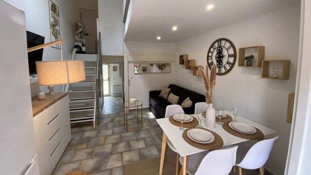 A modern kitchen with white cabinets, a dining table set for four, and a black sofa in the background. - Villa Club Portissol (Sanary-sur-Mer)