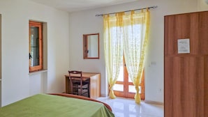A bedroom with a bed, a desk, a chair, a window with curtains, and a door.