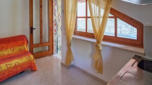 A room with a bed, a window with curtains, a sink, and a tiled floor.