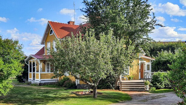 Une maison à deux étages avec un toit rouge, une véranda et un jardin bien entretenu.