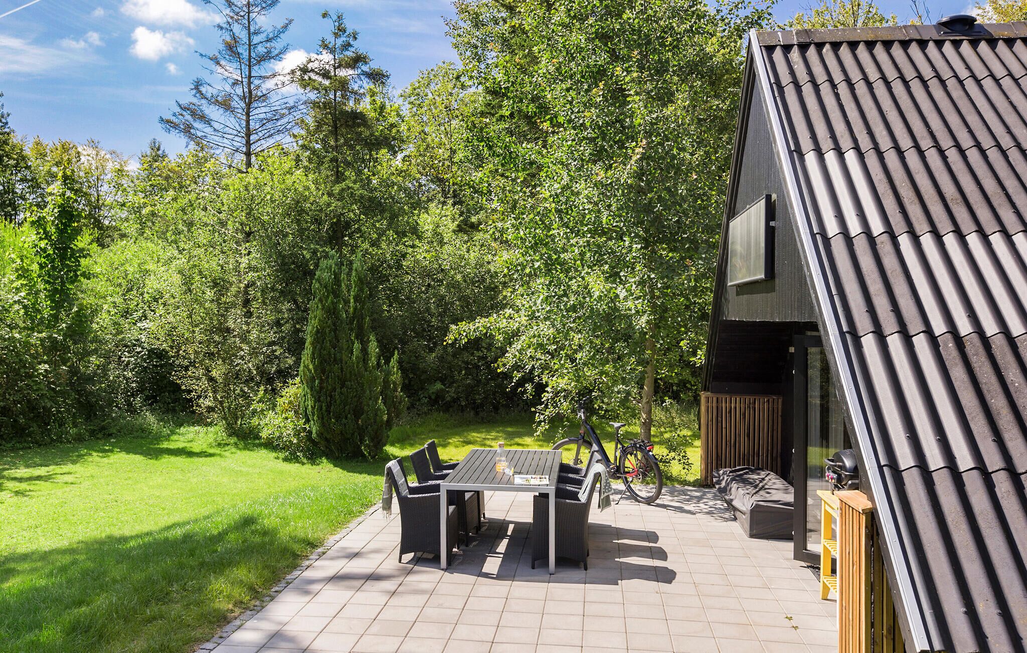 Een terras buiten, met een tafel en stoelen, omgeven door weelderig groen en een houten terras.