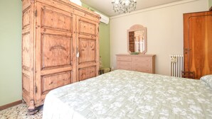 Un dormitorio con un amplio armario de madera, una cama con colcha estampada, un tocador, un espejo y un radiador.