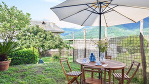 Mesa de madera con sillas y un paraguas grande en un jardín con vistas a montañas.