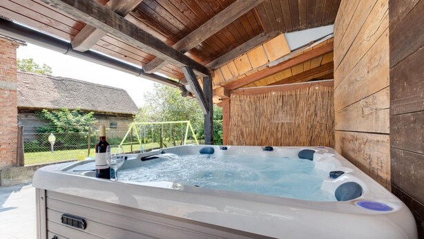 Ein Whirlpool mit Holzdach und Backsteinwänden, umgeben von Zäunen und Grünpflanzen.