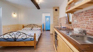 Ein Schlafzimmer mit einem hölzernen Bett, einer kleinen Küchenzeile mit Spüle und einer Backsteinwand.