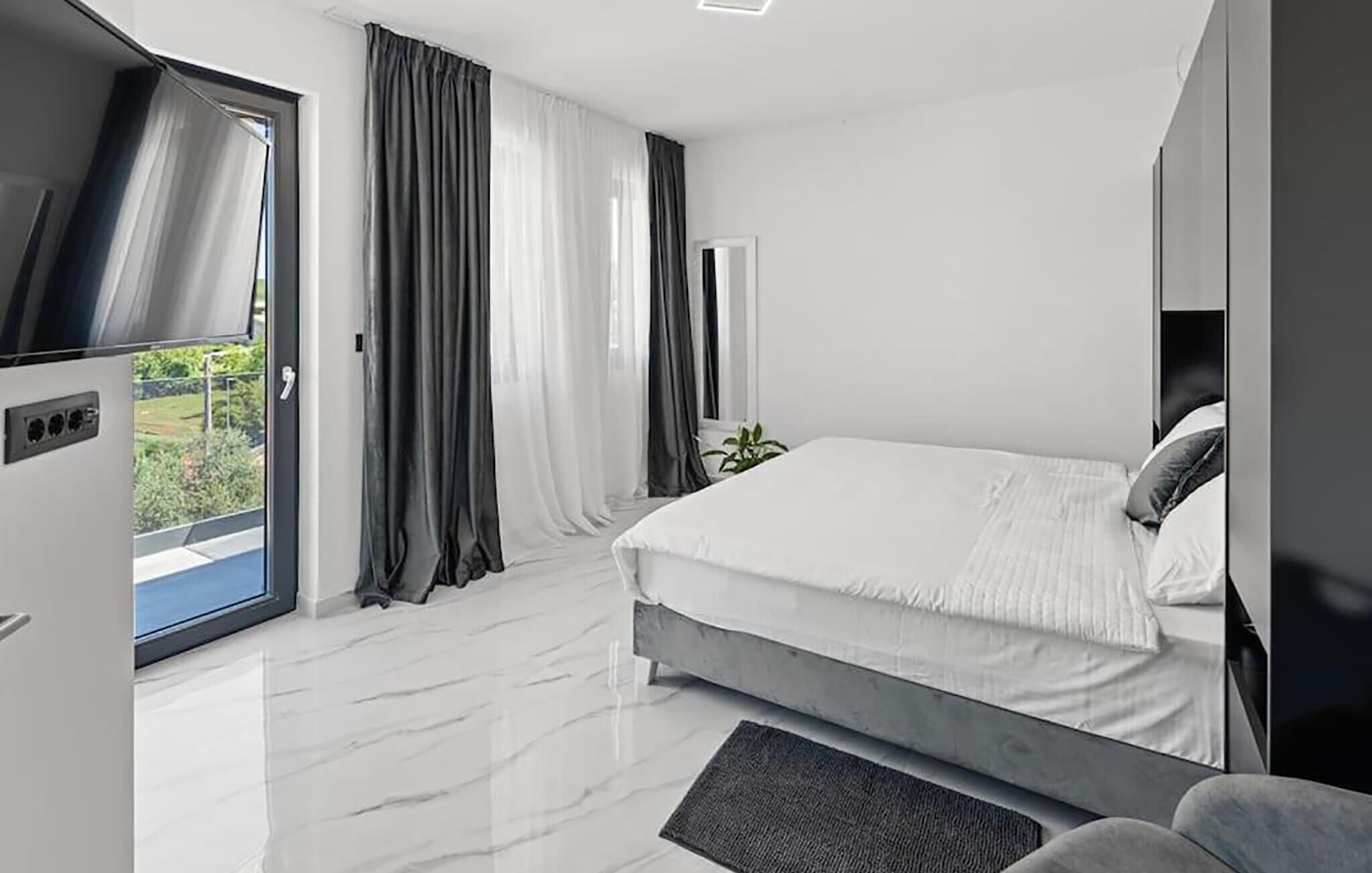 Una camera da letto moderna con un letto, una televisione e vista su piante.