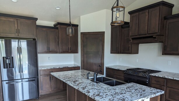 A kitchen with dark wooden cabinets, a stainless steel refrigerator, a granite countertop, a sink, and a gas stove. - Appleton Country home with AC and Wifi (Appleton)