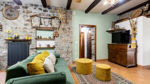 A cozy living room with a stone wall, a green sofa, a wooden cabinet, and a television. - Gorgeous home in Fraz. Cogna, Piazza al (Fraz. Cogna, Piazza al)