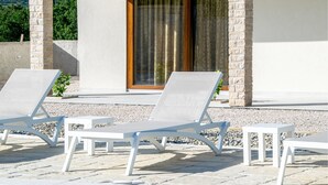 A poolside area with white lounge chairs and a stone wall. - Lovely home in Posedarje (Posedarje)
