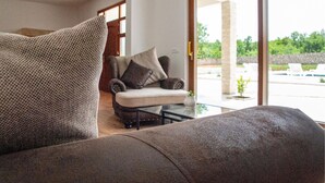 A modern living room with a sofa, a glass coffee table, and a view of a pool and greenery outside. - Lovely home in Posedarje (Posedarje)