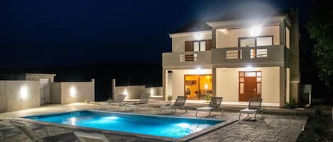 A modern two-story house with a swimming pool and lounge chairs.