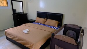 Ein ordentlich bezogenes Bett mit brauner Decke und Kissen, ein Schminktisch und ein Koffer mit einem Kopfkissen.
