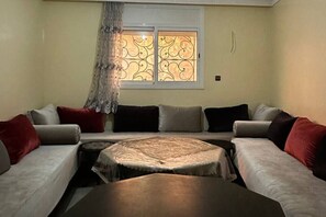 Ein Wohnzimmer mit einer Sofagarnitur, einem runden Couchtisch und einem Fenster mit dekorierter Scheibe.