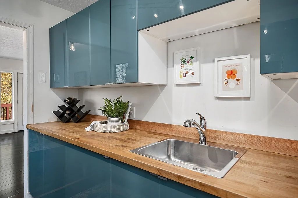 A modern kitchen with teal cabinets, a wooden countertop, a stainless steel sink, and two framed pictures on the wall.