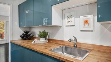 A modern kitchen with teal cabinets, a wooden countertop, a stainless steel sink, and two framed pictures on the wall.