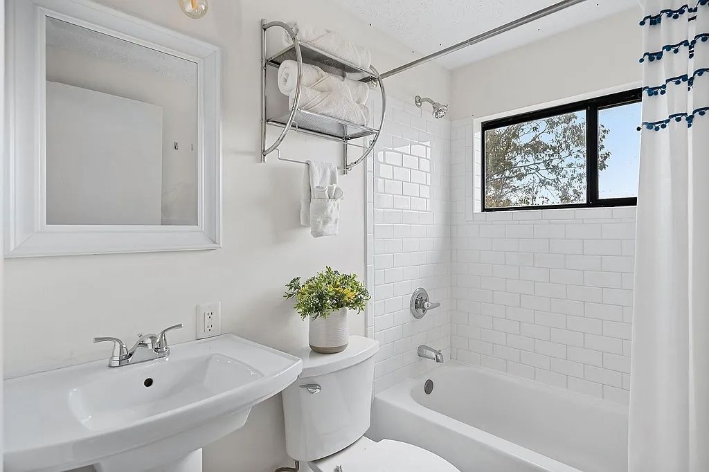 A bathroom with a white sink, toilet, and bathtub, a towel rack, and a window with a view of trees.