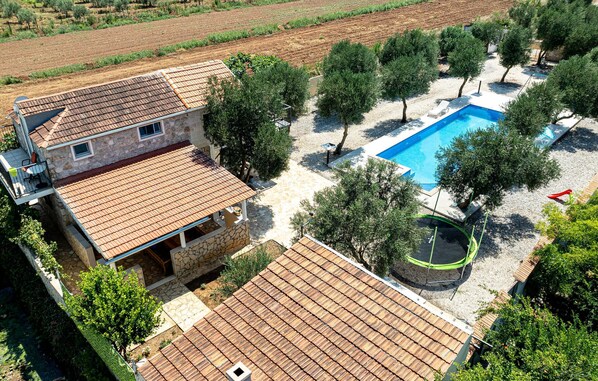 A two-story stone house with a tiled roof, a swimming pool, and surrounding trees. - Stunning home in Ston (Ston)