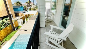 A covered outdoor area with a pool, a white rocking chair, and a view of a blue house in the background. -  Just steps away from the beach, restaurants, stores, and carnival attraction.  (South Padre Island)