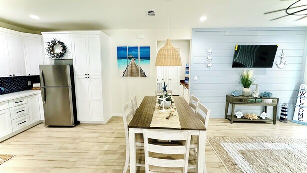 A modern kitchen with white cabinets, a stainless steel refrigerator, and a dining area with a wooden table and white chairs. -  Just steps away from the beach, restaurants, stores, and carnival attraction.  (South Padre Island)