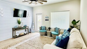 A living room with a sofa, a coffee table, a TV mounted on the wall, a ceiling fan, and a window with blinds. -  Just steps away from the beach, restaurants, stores, and carnival attraction.  (South Padre Island)